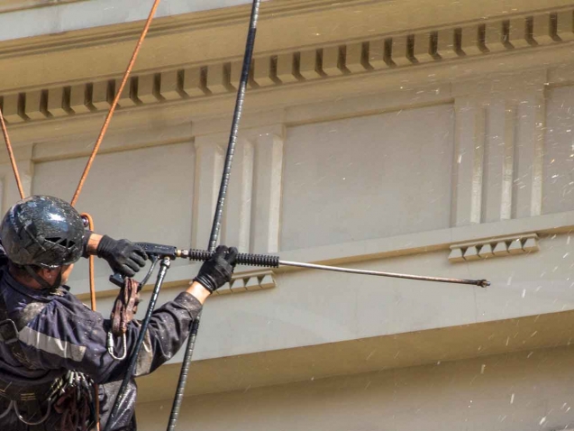 close-up of man hanging off a roof, spraying a difficult to reach location